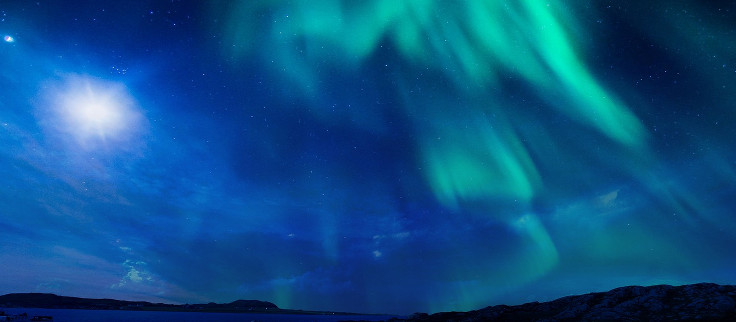 A green aurora seen in Scotland in a large blue night sky just above barely-visible land.